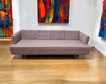 May include: A long, gray tufted sofa with wooden legs. The sofa is in a room with two abstract paintings on the walls.