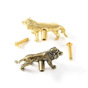 May include: Two lion-shaped cabinet knobs made of metal, one with a bright polished gold finish and the other with an antique brass finish. Each knob features a cylindrical mounting post and is accompanied by a matching threaded metal screw.