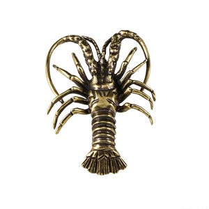 Puede incluir: Una figura de langosta de metal en tono dorado con una cola segmentada detallada, múltiples patas articuladas y largas antenas curvas. La superficie tiene un acabado pulido con áreas oscuras que resaltan la textura del caparazón.