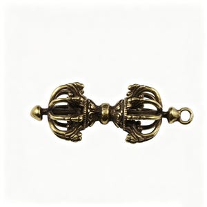 Peut inclure: Un Vajra doré détaillé, un objet rituel aux motifs symétriques et ornés. La partie centrale présente des gravures complexes, avec des extrémités évasées et une boucle à une extrémité. L'objet est posé sur un fond blanc uni.