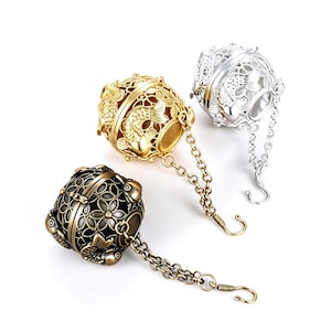 Puede incluir: Tres infusores de té decorativos en oro, plata y bronce. Cada infusor es esférico con intrincados diseños florales y de peces. Cuelgan de cadenas con cierres de gancho, ideales para té de hojas sueltas.
