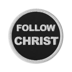 May include: Circular embroidered patch featuring the text "FOLLOW CHRIST" in white on a black background. The patch has a white stitched border. Suitable for attaching to clothing or accessories, offering a simple yet impactful message.