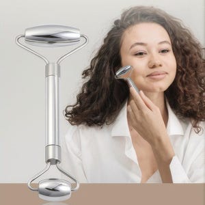 May include: A silver facial roller with a cylindrical handle and rounded roller heads. The roller is held near a person's face, suggesting its use for skincare. The product is designed for facial massage and relaxation.