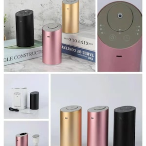 May include: A collection of cylindrical essential oil diffusers in gold, pink, and black. Each diffuser has a slanted top with a button and a small slot. The diffusers are displayed on books and a white surface.