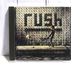 May include: A CD case with a black background and a white tiled wall with the word "RUSH" in black letters. A young person in blue jeans and a black shirt kicks a soccer ball.