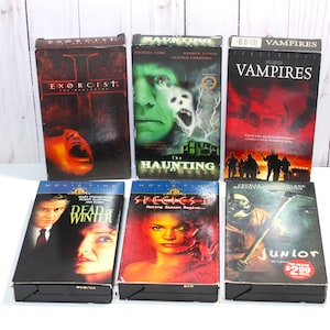 Puede incluir: Una colección de seis cintas VHS con títulos de películas de terror y suspense. Los títulos incluyen "El Exorcista", "The Haunting", "Vampires", "Dead of Winter", "Species II" y "Junior". Las cintas tienen ilustraciones coloridas y se muestran sobre una superficie blanca.