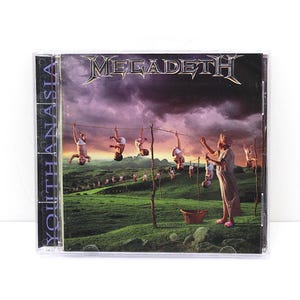 May include: A Megadeth Youthanasia music CD in a clear plastic jewel case. The cover art depicts a person hanging babies from a clothesline in a green field under a dark, stormy purple sky. The band name Megadeth is printed in silver at the top.