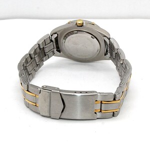 May include: A stainless steel wristwatch with a silver and gold-tone band. The watch has a round face and a clasp closure. The back of the watch is visible, showing the battery compartment and other details. The watch band is approximately 8 inches long.