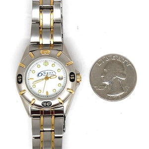 May include: A silver and gold-tone Sigma wristwatch with a white face, featuring black numerals and gold hands. The watch has a date display and is next to a US quarter coin.