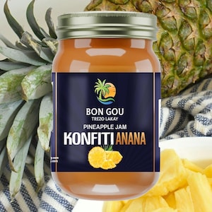 May include: A jar of pineapple jam with a navy blue label featuring the text "BON GOU TREZO LAKAY PINEAPPLE JAM KONFITI ANANA". The jar is filled with a golden-orange jam, and is surrounded by fresh pineapple and pineapple slices.