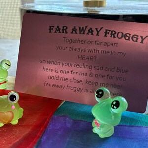May include: Four small, translucent green frog figurines with large black eyes and various details like a bow tie and heart. A pink card with the text "FAR AWAY FROGGY" is in the background.
