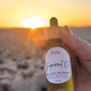 Può includere: Un piccolo flacone contagocce in vetro trasparente contenente olio giallo dorato con un'etichetta bianca che riporta la scritta Desert We Roast Chaparral Oil, 100% Natural and Handmade, Net 1 oz. Il flacone ha un tappo in legno ed è pieno.