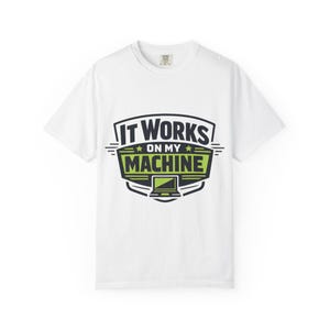 May include: White crew neck t-shirt with the slogan "IT WORKS ON MY MACHINE" in a black, green, and white graphic. The design includes a laptop icon. The shirt is made of a soft material.
