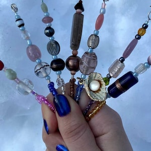 May include: A collection of seven beaded jewelry pieces, each with a unique design and color palette. The beads include various shapes and materials, such as glass, gemstones, and metal. The pieces are held together, showcasing a variety of styles.