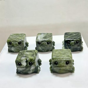 May include: A white ceramic mug with a black handle and the text "But First, Coffee" in a bold, black font. The mug is set against a blurred background, suggesting a cozy setting.