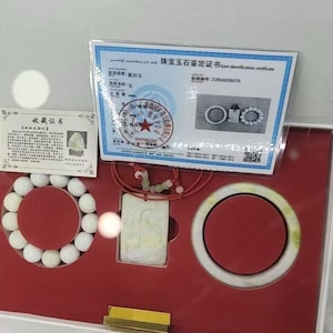 May include: A white jade jewelry set in a red-lined display box, including a beaded bracelet, a rectangular pendant on a red cord, and a bangle. The set includes two paper certificates with Chinese text and a gem identification certificate.