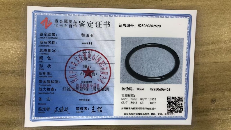 May include: A white rectangular gemstone identification certificate featuring a blue border, a photograph of a black circular bangle, Chinese text, a red circular stamp, a QR code, and the certificate number N25060602598 printed in black ink.