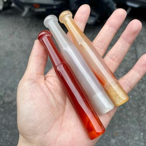 May include: Three smooth, cylindrical, rod-like objects with rounded ends, crafted from translucent material. One is a deep, solid red, one is a milky, semi-transparent white, and the third is a warm, light amber or honey-toned yellow colour.