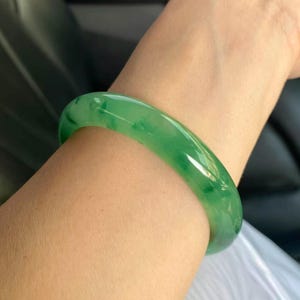 Può includere: Un braccialetto bangle di giada verde brillante. La pietra lucida e traslucida mostra diverse tonalità di verde. La forma liscia e arrotondata del braccialetto è progettata per essere indossata al polso. La giada è una pietra naturale.