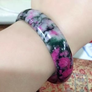 May include: A smooth, polished bangle bracelet featuring a mottled pattern of vibrant magenta, deep forest green, and white mineral inclusions. The circular band has a rounded profile and a glossy finish, displaying a natural stone texture.