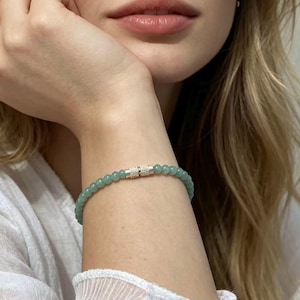 May include: A beaded bracelet featuring small, round, light green beads. The bracelet has a silver-colored clasp. The beads are strung together to form a delicate piece of jewelry.