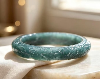 May include: A translucent, deep green jade bangle bracelet featuring intricate, hand-carved relief patterns of swirling clouds and dragon-like motifs encircling the entire outer surface of the polished, circular stone band.