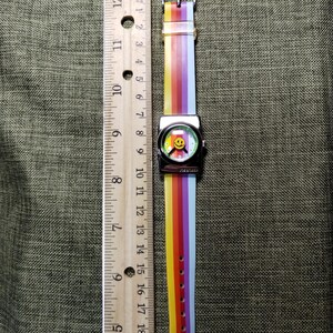May include: A colorful watch with a rainbow striped band and a smiley face on the watch face. The watch band is approximately 9 inches long. The watch face is silver with the word "JOE BOXER" printed on the watch face.
