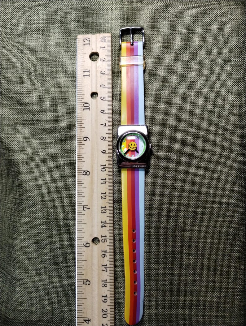 May include: A colorful watch with a rainbow striped band and a smiley face on the watch face. The watch band is approximately 9 inches long. The watch face is silver with the word "JOE BOXER" printed on the watch face.