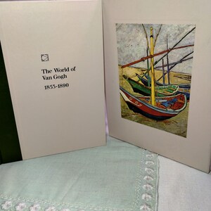 May include: A hardcover book titled The World of Van Gogh 1853-1890 with a cream-colored cover and a small square logo. Beside it, a matching cream-colored slipcase features a reproduction of a painting depicting colorful fishing boats.