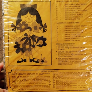 May include: Vintage craft kit packaging featuring a girl holding flowers, with the word "DESIGNS" at the top. The kit is labeled "FLORA" and measures 2' x 3'. Includes color schemes and tufting instructions. The packaging is yellow.