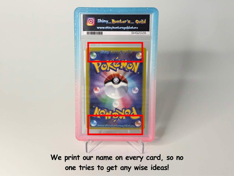 May include: A graded Pok&eacute;mon trading card encased in a blue and pink plastic slab. The card back features the Pok&eacute;mon logo, a central Pok&eacute; Ball graphic, and the text Shiny Hunter's Guild printed at the top and bottom within the card design.