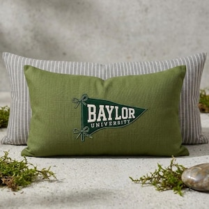 Peut inclure: Un coussin rectangulaire vert olive orné d'un fanion brodé vert foncé avec le texte Baylor University en blanc. Le coussin est placé devant un coussin rectangulaire plus grand à rayures verticales grises et blanches.