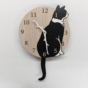 May include: A wooden wall clock featuring a black and white cat silhouette. The clock face is a light wood color with black numerals and white hands. The cat's tail serves as the clock's pendulum, adding a playful touch to the design.