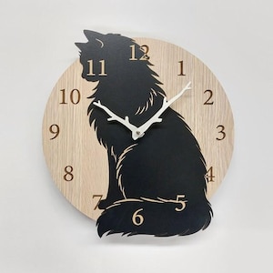 Könnte beinhalten: Eine Wanduhr aus Holz mit einer schwarzen Katzen-Silhouette. Das Zifferblatt ist helles Holz mit schwarzen Ziffern und weißen Zeigern. Die Katze sitzt mit eingerolltem Schwanz.