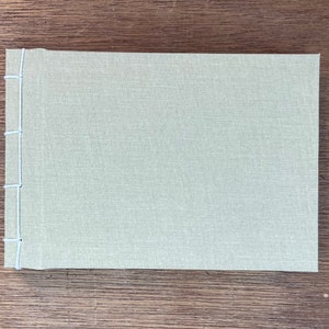 May include: A light green fabric-covered journal with white stitching along the spine.