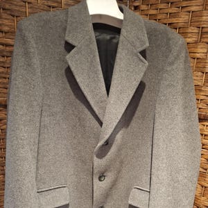 May include: A gray wool coat with a classic design. The coat features a notched lapel, three buttons, and two front pockets. The coat is hanging on a white hanger.