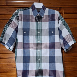 Pode incluir: Uma camisa de botões de manga curta, em xadrez branco, azul, verde e roxo.