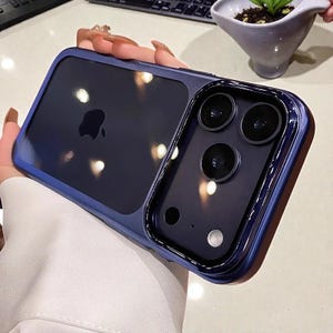 May include: A dark blue smartphone case featuring a smooth, glossy finish and a raised frame around the camera module. The case has a cutout for the Apple logo on the back and a rectangular opening for the triple-lens camera system and flash.