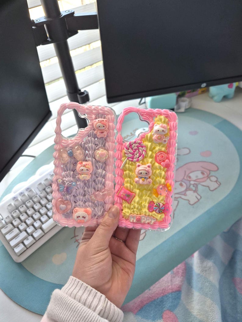 May include: Two decorative phone cases. One is pink and purple with charms, including a bear, butterflies, and flowers. The other is pink and yellow with a bear, candy, and the word "Happy".
