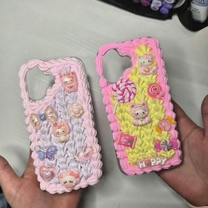 May include: Two decorative phone cases. One is light pink with a textured border and various embellishments, including a bow, a butterfly, and a heart. The other is yellow with a pink border, featuring a cat, candies, and the word "HOPPY".