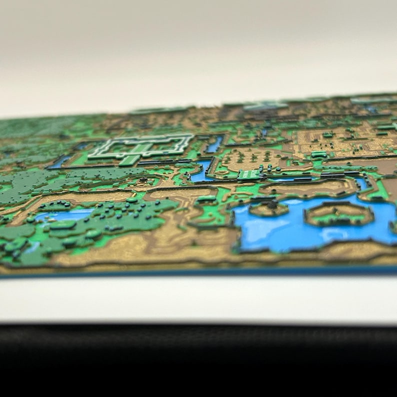 May include: A detailed, three-dimensional map featuring a landscape with green, brown, and blue elements. The map appears to be a stylized representation of a geographical area, with raised features and water bodies. The color palette includes shades of green, brown, and blue.