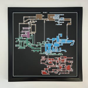 May include: A framed wall art piece featuring a stylized map of Zebes on a black background. The map consists of interconnected geometric sections in shades of brown, purple, green, blue, and red, with the text ZEBES printed at the top center.