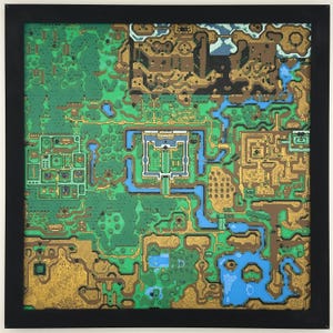 May include: A framed, colorful map of a fantasy world. The map features green forests, blue waterways, and gold-colored structures. The artwork is encased in a black frame, creating a striking visual contrast. The map's intricate details suggest a game or fictional setting.