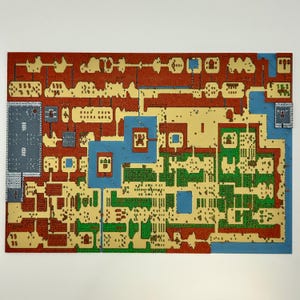 May include: A rectangular wall art piece featuring a multi-layered, top-down 2D map design. The map displays a grid-like landscape with distinct sections in red, beige, green, and blue, representing various terrain types and structures.