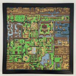 May include: A framed, colorful map of a video game world. The map features a detailed landscape with green fields, brown mountains, blue water, and various structures. The frame is black, and the overall aesthetic is reminiscent of a classic video game.