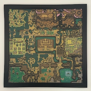 May include: A framed, colorful map print with a black border. The map features a detailed, stylized landscape with green, brown, gold, and pink hues, depicting what appears to be a fantasy world or game environment. The artwork is square.