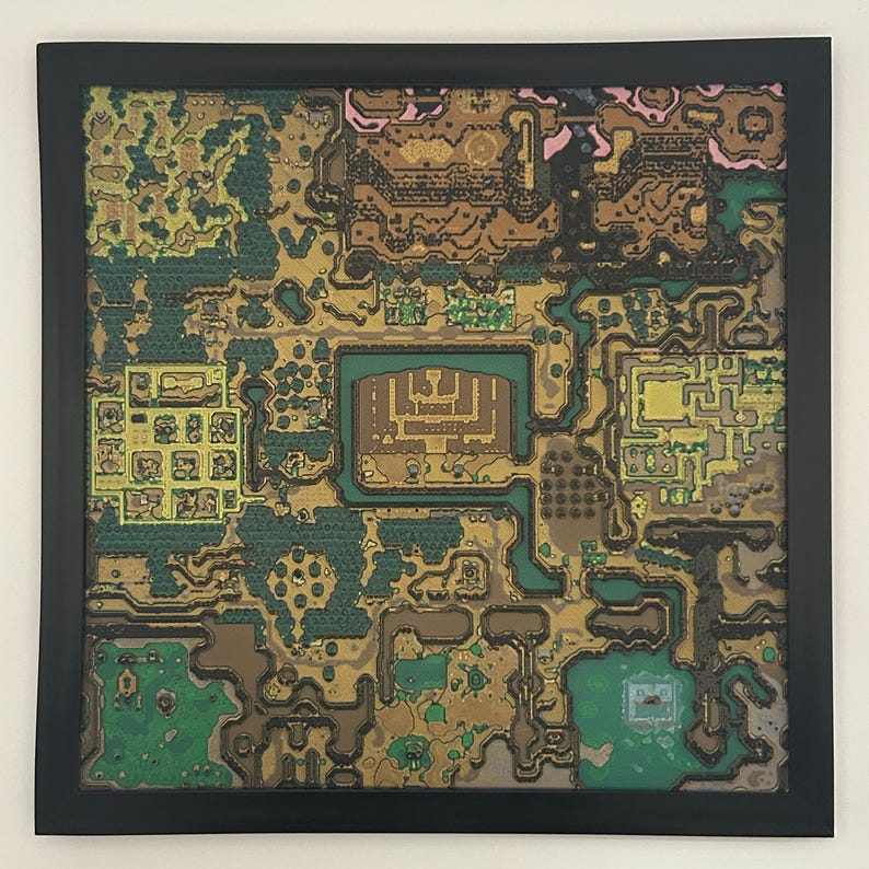 May include: A framed, colorful map print with a black border. The map features a detailed, stylized landscape with green, brown, gold, and pink hues, depicting what appears to be a fantasy world or game environment. The artwork is square.