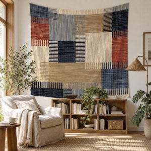 May include: A large rectangular wall tapestry featuring a geometric patchwork design in shades of navy blue, rust red, and beige. The pattern consists of alternating solid and striped blocks with a textured appearance, hanging flat against a wall.