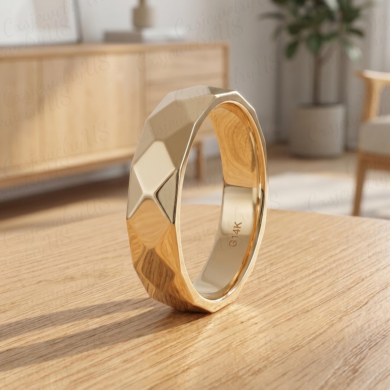 May include: A gold-colored ring with a geometric, faceted design. The ring has a flat band and a series of angled surfaces that create a textured appearance. The interior of the ring is smooth. The ring is marked with "G14K".