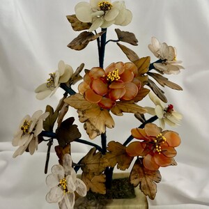 May include: A decorative bonsai-style sculpture featuring translucent white and amber-colored stone flowers with yellow centers. The plant has brown stone leaves and dark stems, all anchored in a square, light green stone pot base.